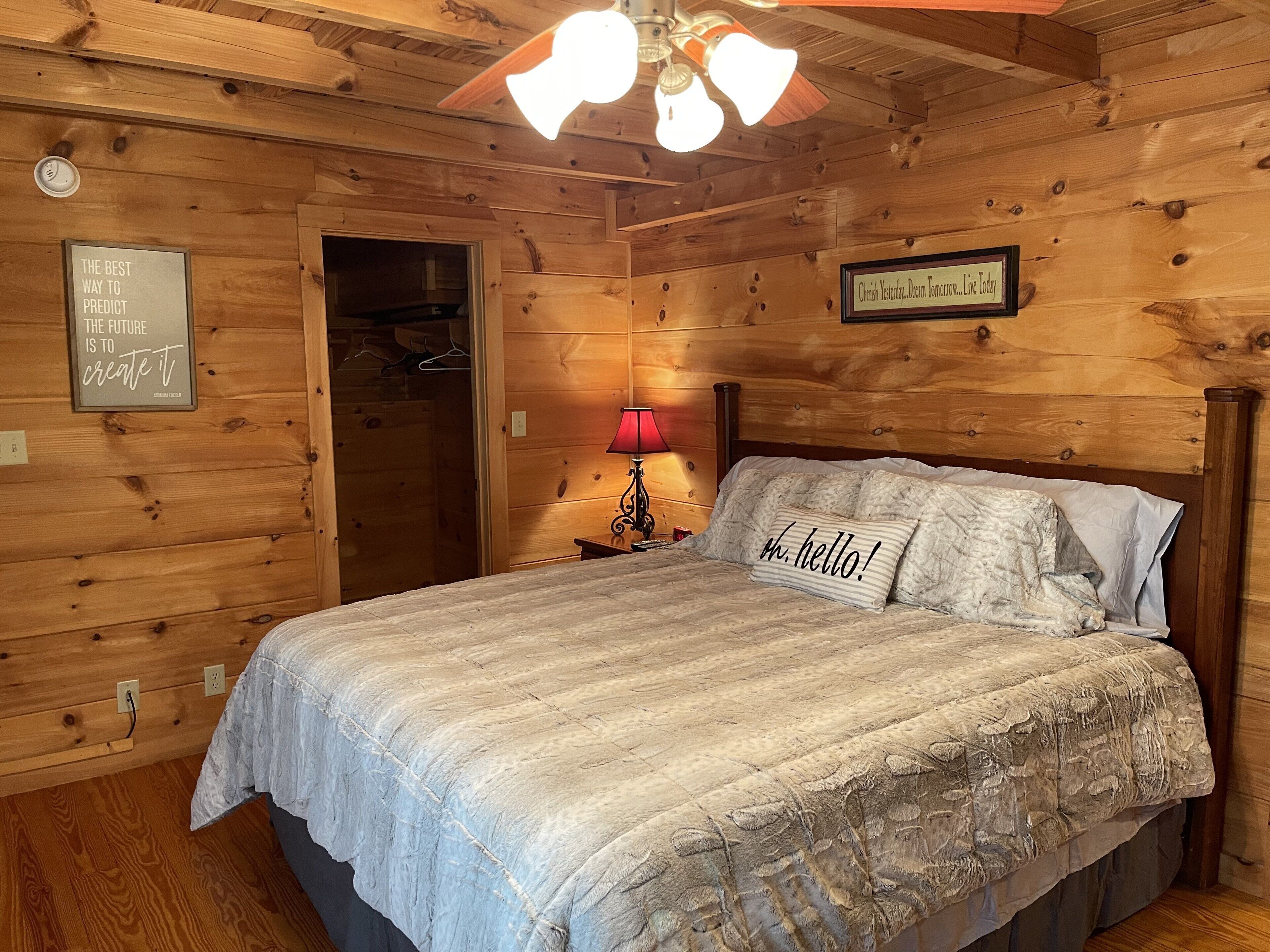 A cozy wooden room with a bed, a nightstand, a lamp, and a motivational quote on the wall.