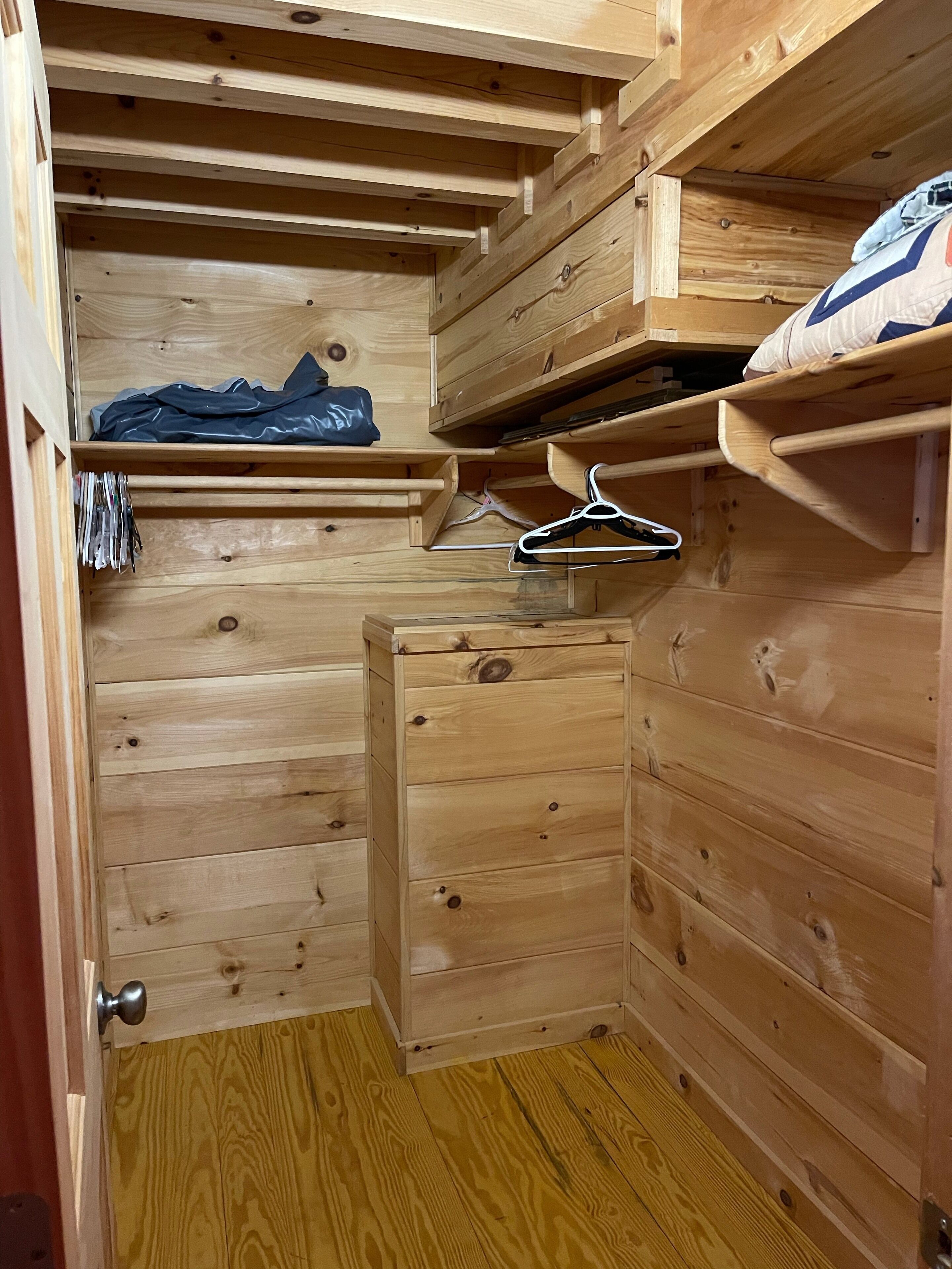 A wooden room with a built-in wardrobe, a small bench, and a shelf with a bag.