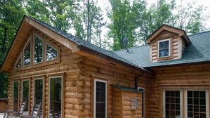 A log cabin with large windows, a deck with chairs, and a picnic table.