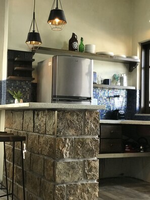 Et køkken med en stenø, stålstål-hvidevarer, hængende pendellamper og et backsplash med mosaikfliser.
