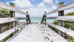 Un paseo marítimo de madera que lleva a una playa con agua turquesa cristalina y un cielo despejado.