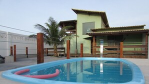 A swimming pool with a pink floatation device, surrounded by a concrete deck. - CASA DE FRENTE PARA A PRAIA DE FIGUEIRA COM PISCINA - ARRAIAL DO CABO (Arraial do Cabo)