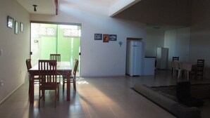 A spacious living area with a dining table and chairs, a sofa, and a refrigerator. - CASA DE FRENTE PARA A PRAIA DE FIGUEIRA COM PISCINA - ARRAIAL DO CABO (Arraial do Cabo)