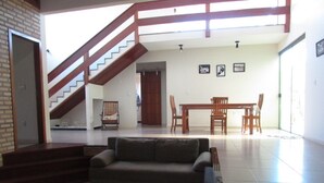 A spacious living area with a staircase, a sofa, a dining table with chairs, and a wooden door. - CASA DE FRENTE PARA A PRAIA DE FIGUEIRA COM PISCINA - ARRAIAL DO CABO (Arraial do Cabo)