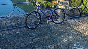 Una bicicleta estacionada en un área empedrada con vista a un río y follaje.