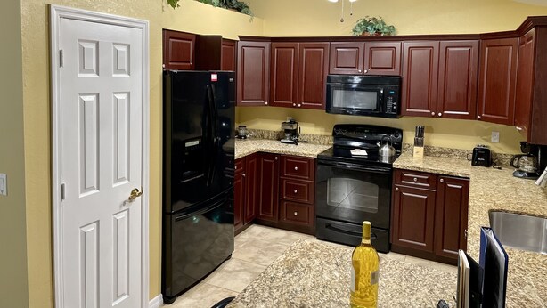 Una cucina con mobili in legno scuro, un frigorifero nero, un forno a microonde, un fornello e una ventola a soffitto.