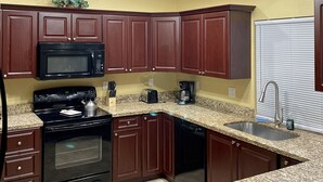 Una cucina con pensili in legno scuro, un forno a microonde nero, un piano cottura e una ventola a soffitto.