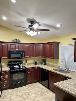 A kitchen with dark wooden cabinets, a black microwave, a stove, and a ceiling fan. - LOCATION! LOCATION! CENTRALLY LOCATED ! (Cape Coral)