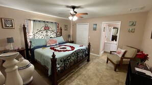 Una camera da letto con un letto, una ventola a soffitto, un comodino, una cassettiera e una sedia.