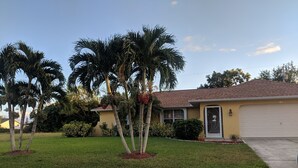 Una casa residenziale con un prato curato, palme e un garage.