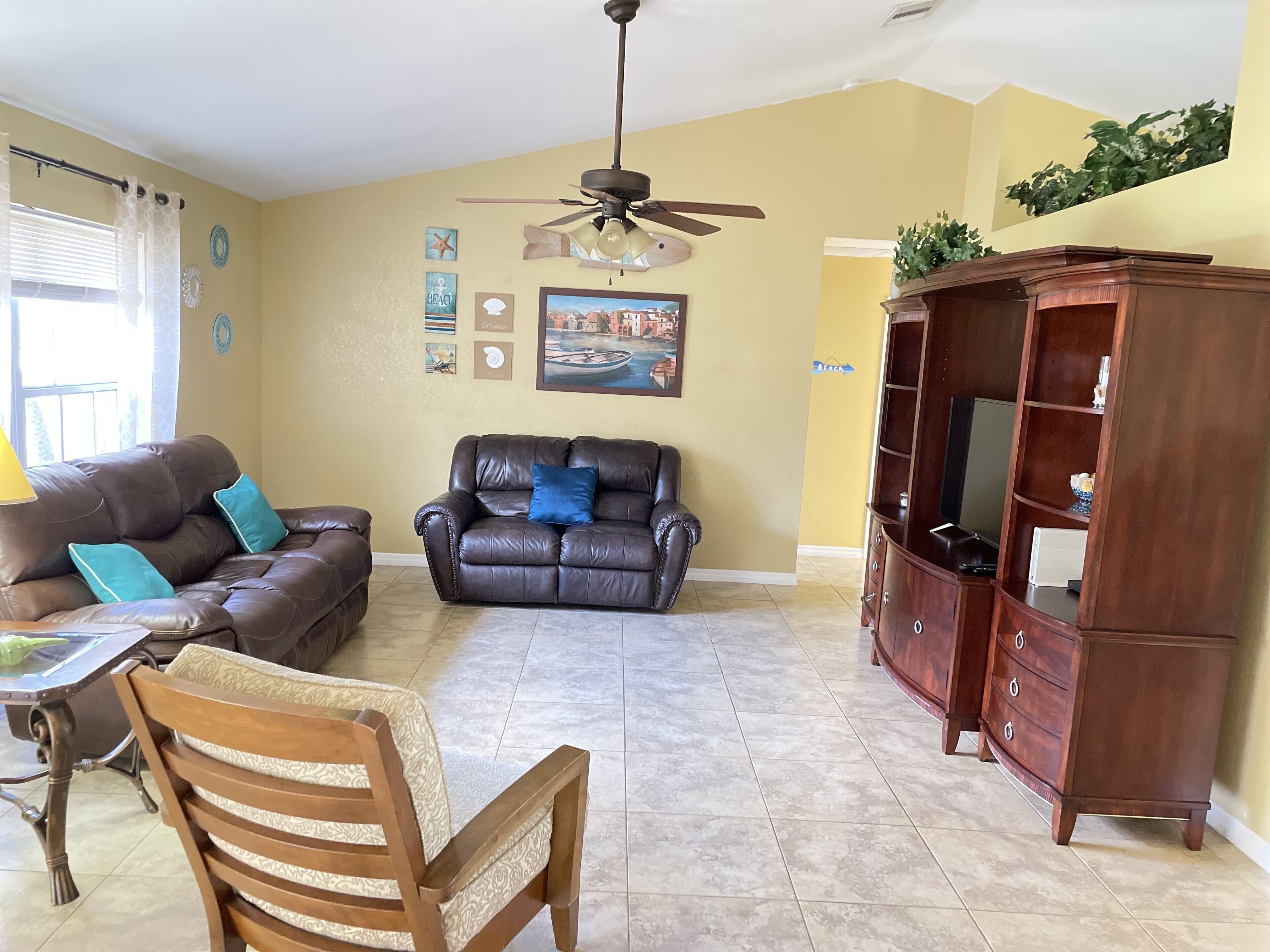 A living room with a brown leather sofa, a wooden chair, a wooden cabinet, and a ceiling fan.