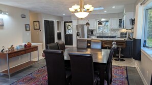 A modern kitchen with a central island, pendant lighting, and a dining area with a patterned rug. - Amazing Lake House With All Amenities (Remsen)