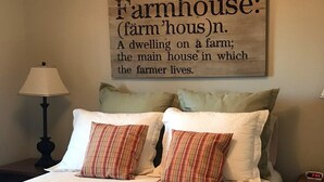 A bedroom with a bed, pillows, a lamp, and a wall-mounted sign defining 'Farmhouse'. - Charming cottage on 65 rolling acres (Mt. Juliet)
