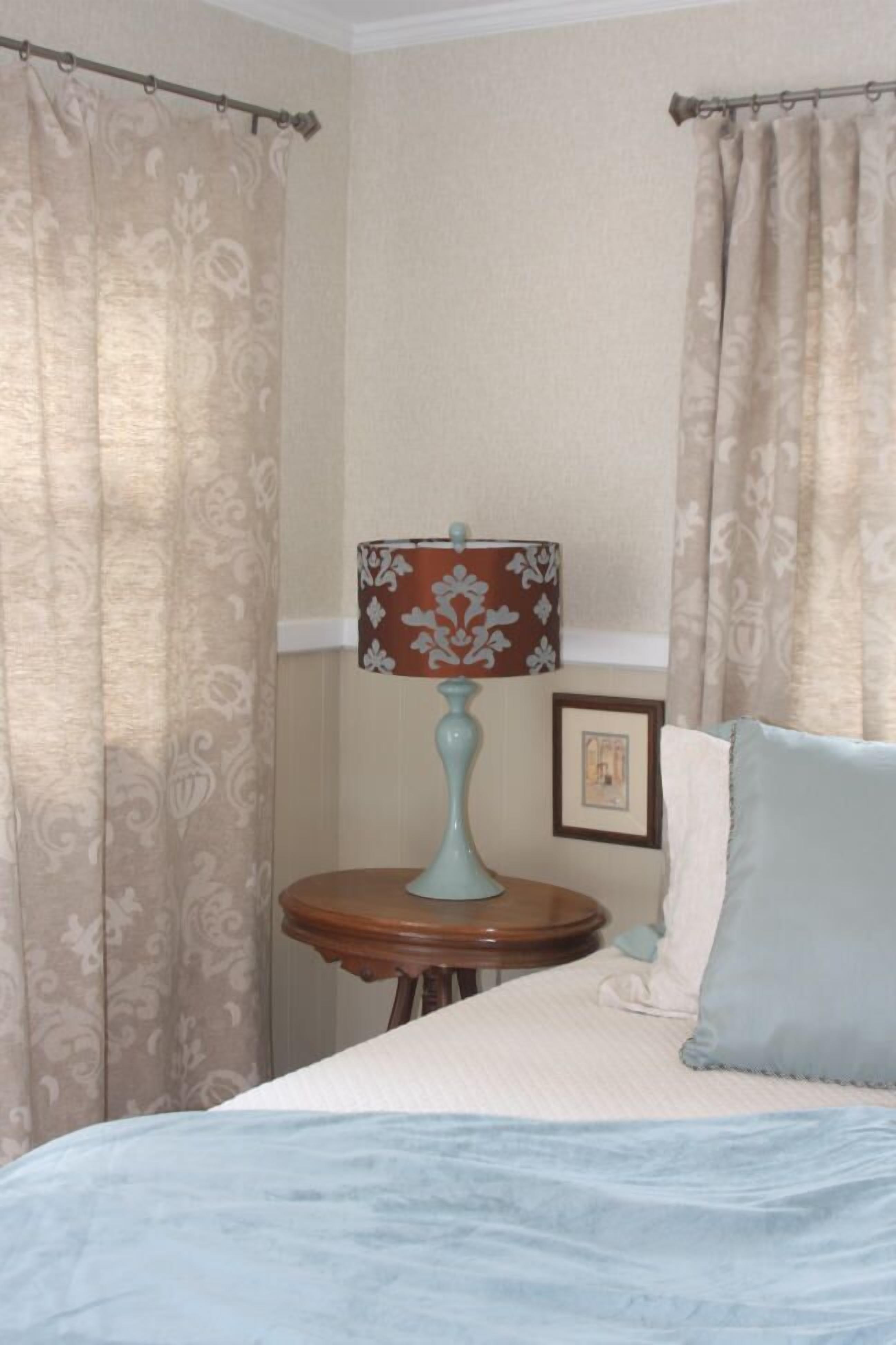 A bedroom with a bed, a lamp, curtains, and a small table.