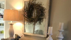 A wooden console table with a lamp, candles, a bird figurine, a mirror, and a woven basket. - Charming cottage on 65 rolling acres (Mt. Juliet)