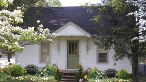 A white house with a green door, surrounded by a garden with various plants and flowers. - Charming cottage on 65 rolling acres (Mt. Juliet)