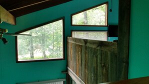Ein Zimmer mit türkisfarbenen Wänden, einer Holzzieldecke und Blick auf einen Wald durch ein großes Fenster.