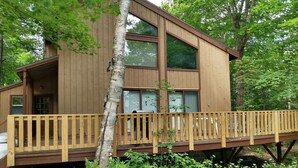 Eine Holzhütte mit einer Terrasse, großen Fenstern und einer naturbelassenen Waldumgebung.