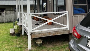 A covered porch with a railing, a car parked nearby, and a wooden fence in the background. - Cozy two story hideaway (Whangamata)