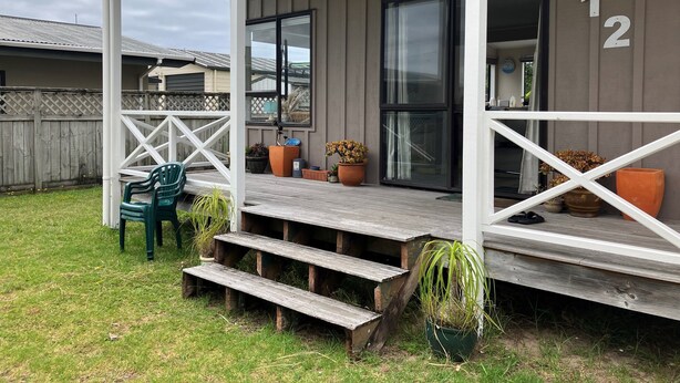 A covered porch with a wooden staircase leading to a door marked "212". - Cozy two story hideaway (Whangamata)