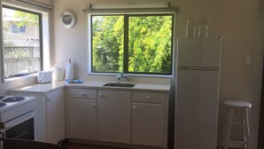 A compact kitchen with a window, a refrigerator, a stove, and a sink. - Cozy two story hideaway (Whangamata)