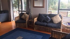 A living room with wicker furniture, a blue sofa, and a blue rug. - Cozy two story hideaway (Whangamata)