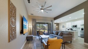 A spacious living area with a sofa, coffee table, and chairs, a kitchen with modern appliances, and a large window offering a view of the outdoors.