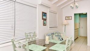 A dining area with a glass table, green chairs, a candle centerpiece, and a view of a kitchen through an open door. - Plumbago - Paradise in the Bahamas with Ocean views (George Town)