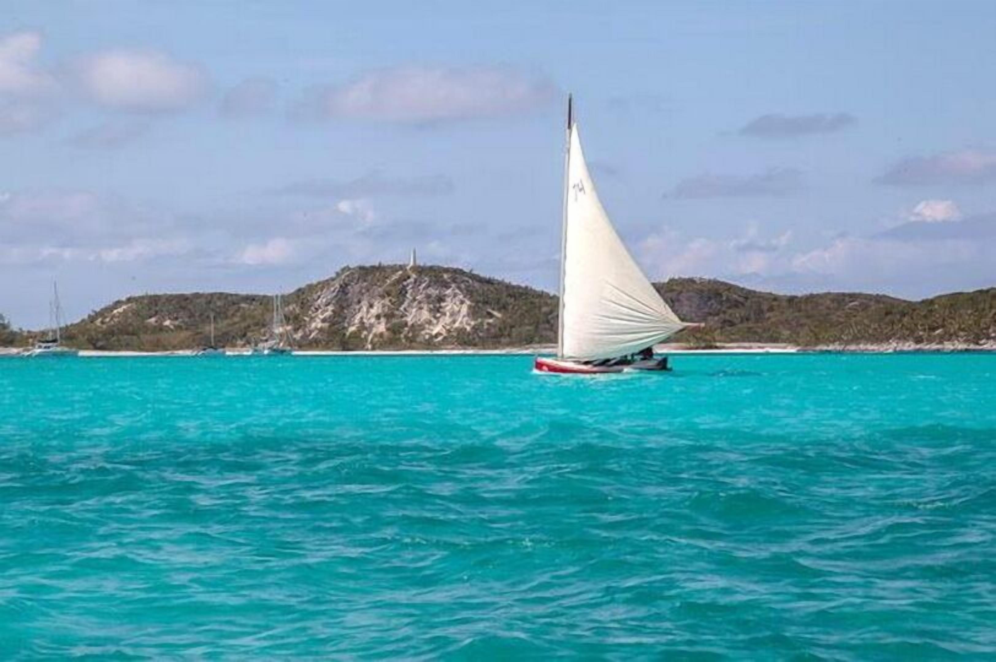 Ein Segelboot auf türkisfarbenem Wasser vor einer bergigen Küstenlinie.