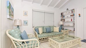 A living room with wicker furniture, a glass coffee table, and a bookshelf. - Plumbago - Paradise in the Bahamas with Ocean views (George Town)