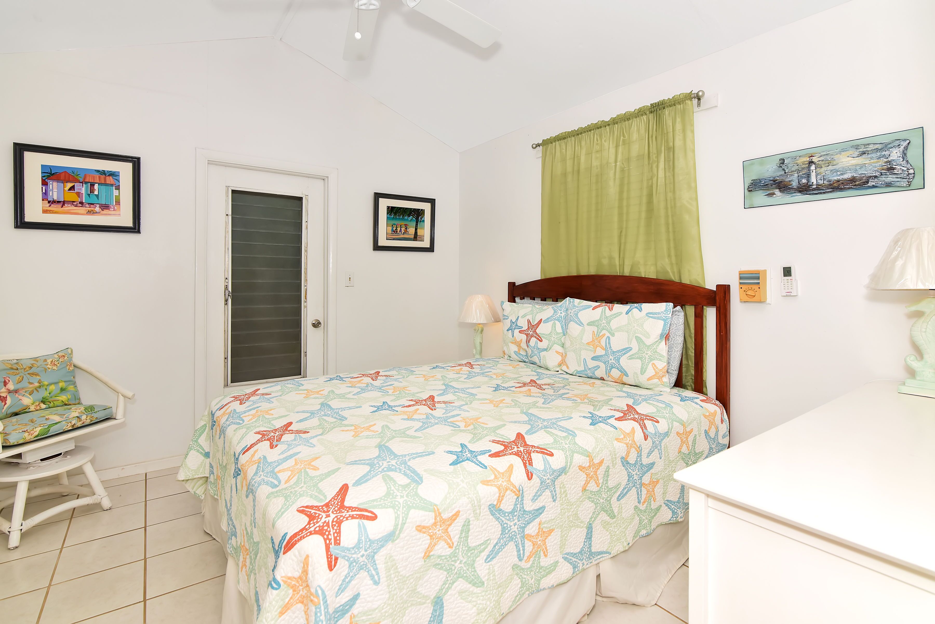 A bedroom with a bed, a chair, a desk, and artwork on the walls.