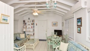 A spacious living room with a high ceiling, a chandelier, a ceiling fan, a bookshelf, a TV, and a dining area with a glass table and chairs. - Plumbago - Paradise in the Bahamas with Ocean views (George Town)