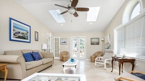 A spacious living room with a beige sofa, a white coffee table, wicker chairs, and a ceiling fan. - Albion by Seaside Vacations & Sales (Chincoteague Island)