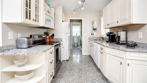 A kitchen with white cabinets, granite countertops, a toaster, a coffee maker, and a refrigerator. - Albion by Seaside Vacations & Sales (Chincoteague Island)