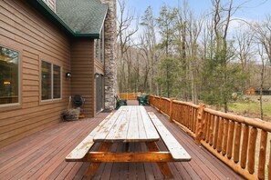 Eine Holzterrasse mit Picknicktisch und -stühlen, umgeben von einem Steinhaus und einem Holzzaun.