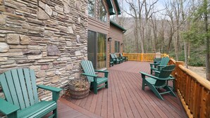 Un mur extérieur en pierre, une terrasse en bois et des fauteuils Adirondack verts.