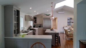 Cozinha moderna com ilha central, área de refeições com uma cadeira e vista para a sala de estar.