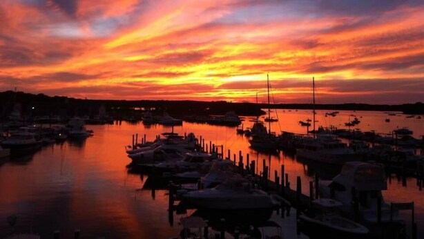 Uma marina ao pôr do sol, com barcos atracados e uma superfície de água calma refletindo o céu.