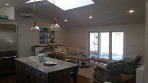 Uma cozinha espaçosa com ilha central, iluminação pendente e uma grande porta de vidro deslizante que dá para um alpendre.