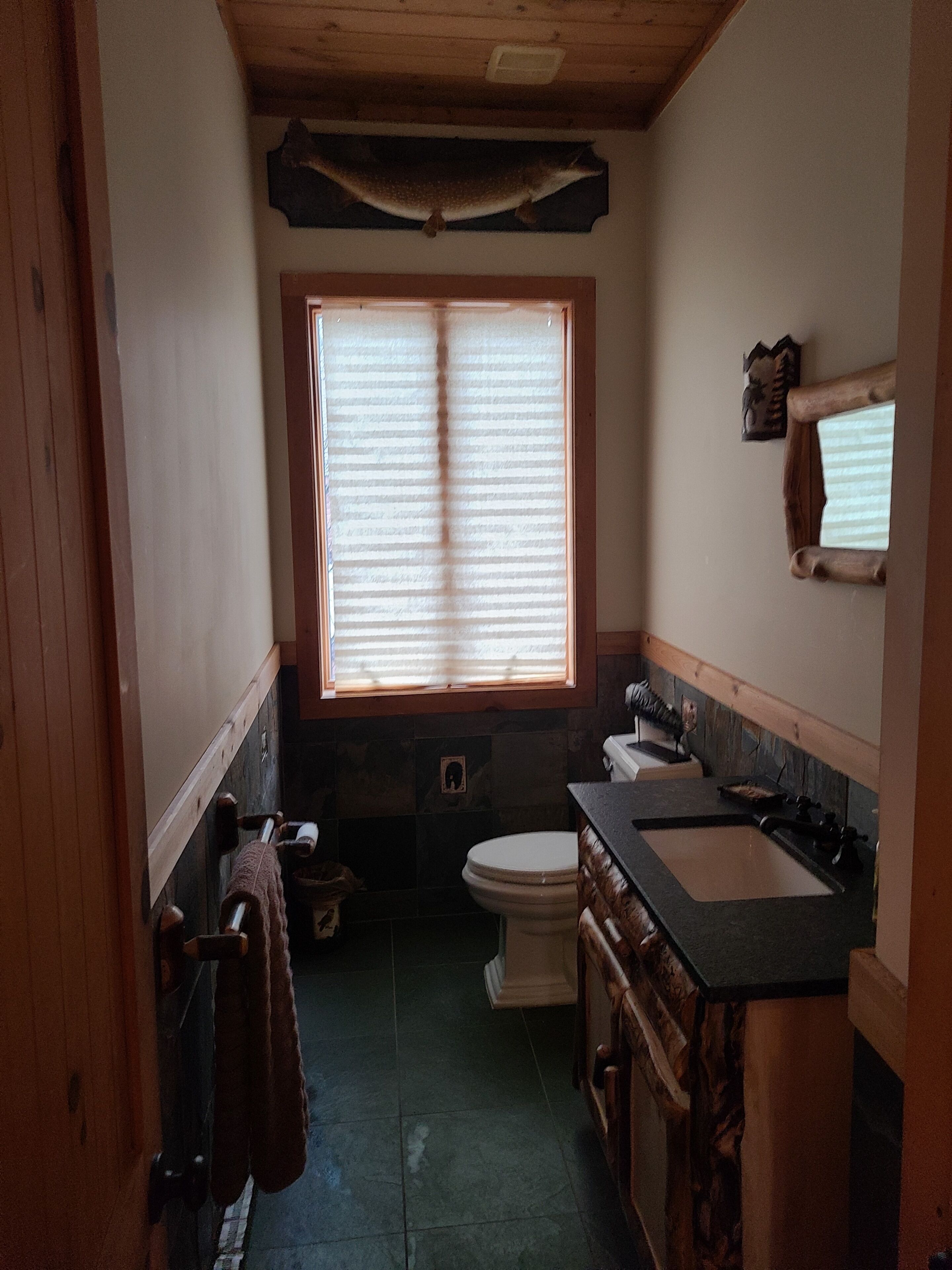 Un baño pequeño y rústico con ventana, inodoro, lavabo y toallero.