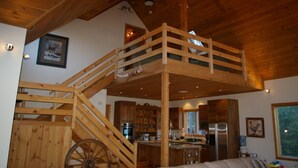 Un intérieur en bois avec une chambre à coucher située en mezzanine, une cuisine et une grande fenêtre.