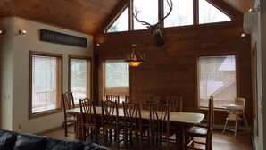 Un coin repas avec une grande table et des chaises en bois, un lustre et une tête de cerf accrochée au mur.