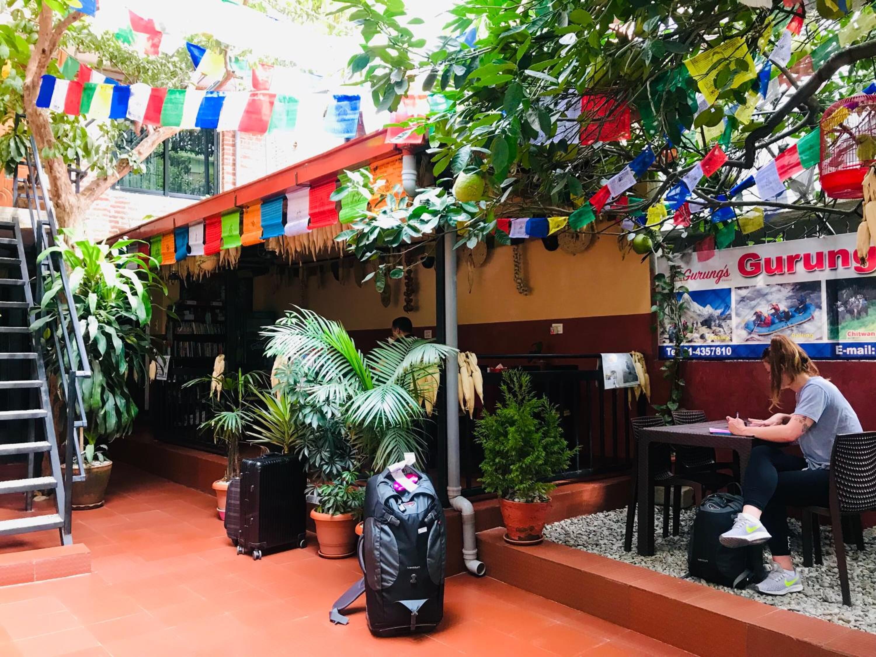 A courtyard with potted plants, a staircase, and a table with a person sitting.