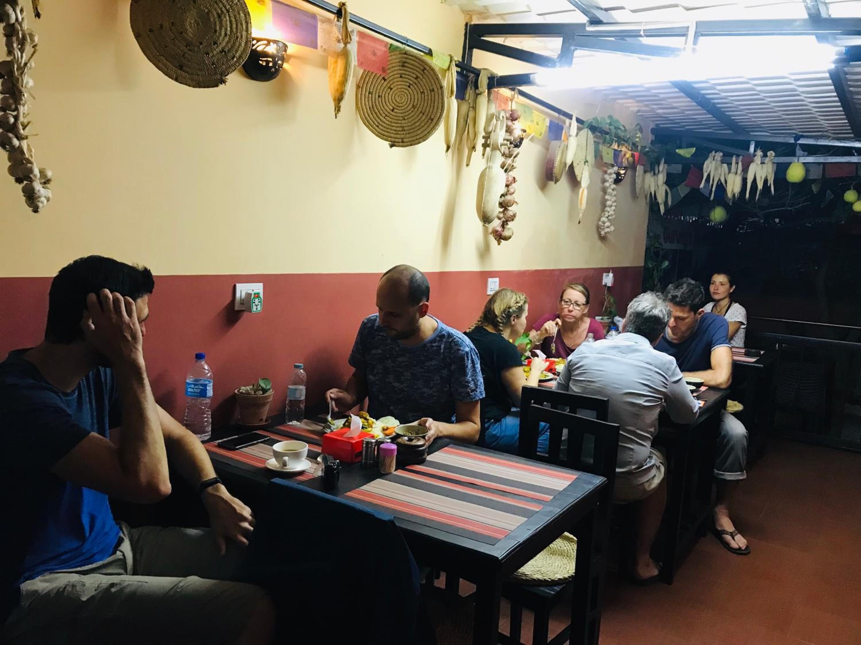 A group of people dining in a restaurant with a simple layout, featuring tables and chairs, and a ceiling with a grid pattern.