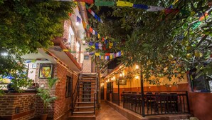 A cozy indoor courtyard with a brick wall, a staircase, and a seating area with tables and chairs. - Gurung's Home (Kathmandu)