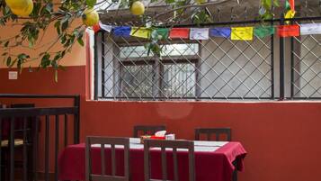 A dining area with a table set for four, surrounded by chairs, under a tree with lemons.