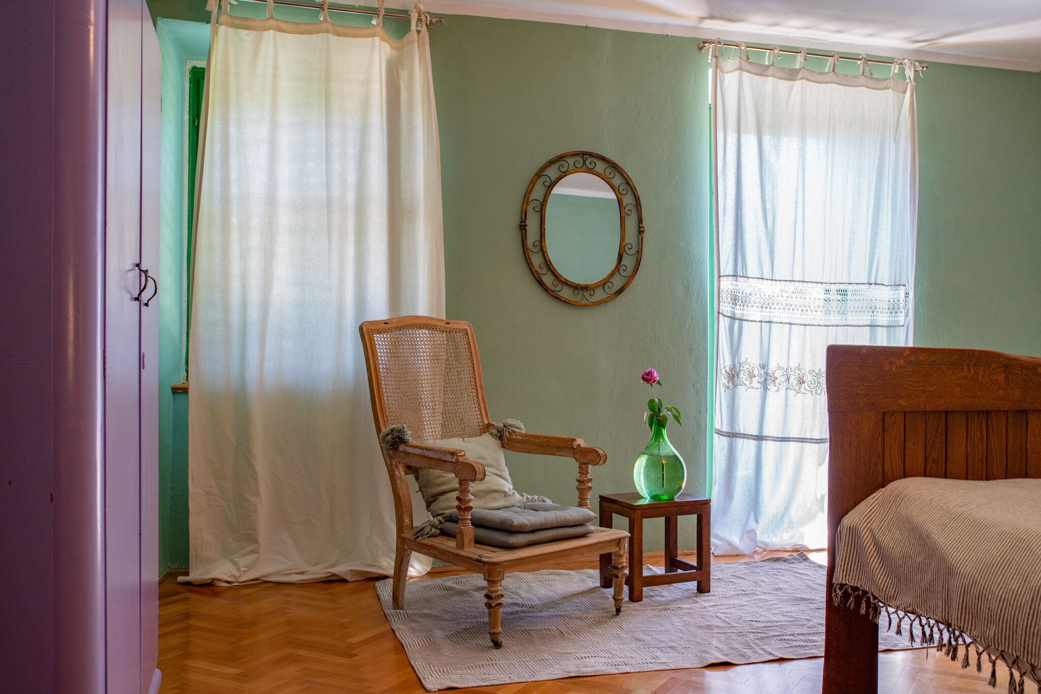 Ein Zimmer mit einem hölzernen Bett, einem Holzstuhl, einem kleinen Tisch mit einer Vase und einem Spiegel an der Wand.