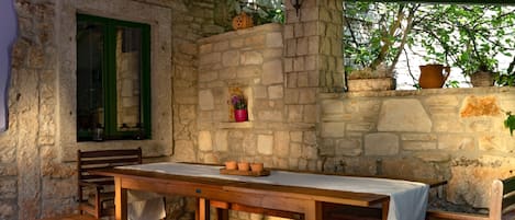 A rustic stone wall with a window, a wooden table with a bench, and potted plants.
