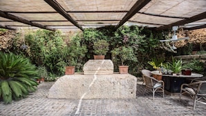 En overdækket patio med en stenpyramide, fletmøbler og krukker med planter.
