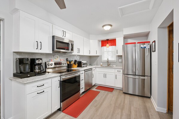 A modern kitchen with white cabinets, stainless steel appliances, and a red accent wall.
